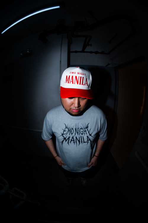 Person wearing a cap and t-shirt with text in a dark setting