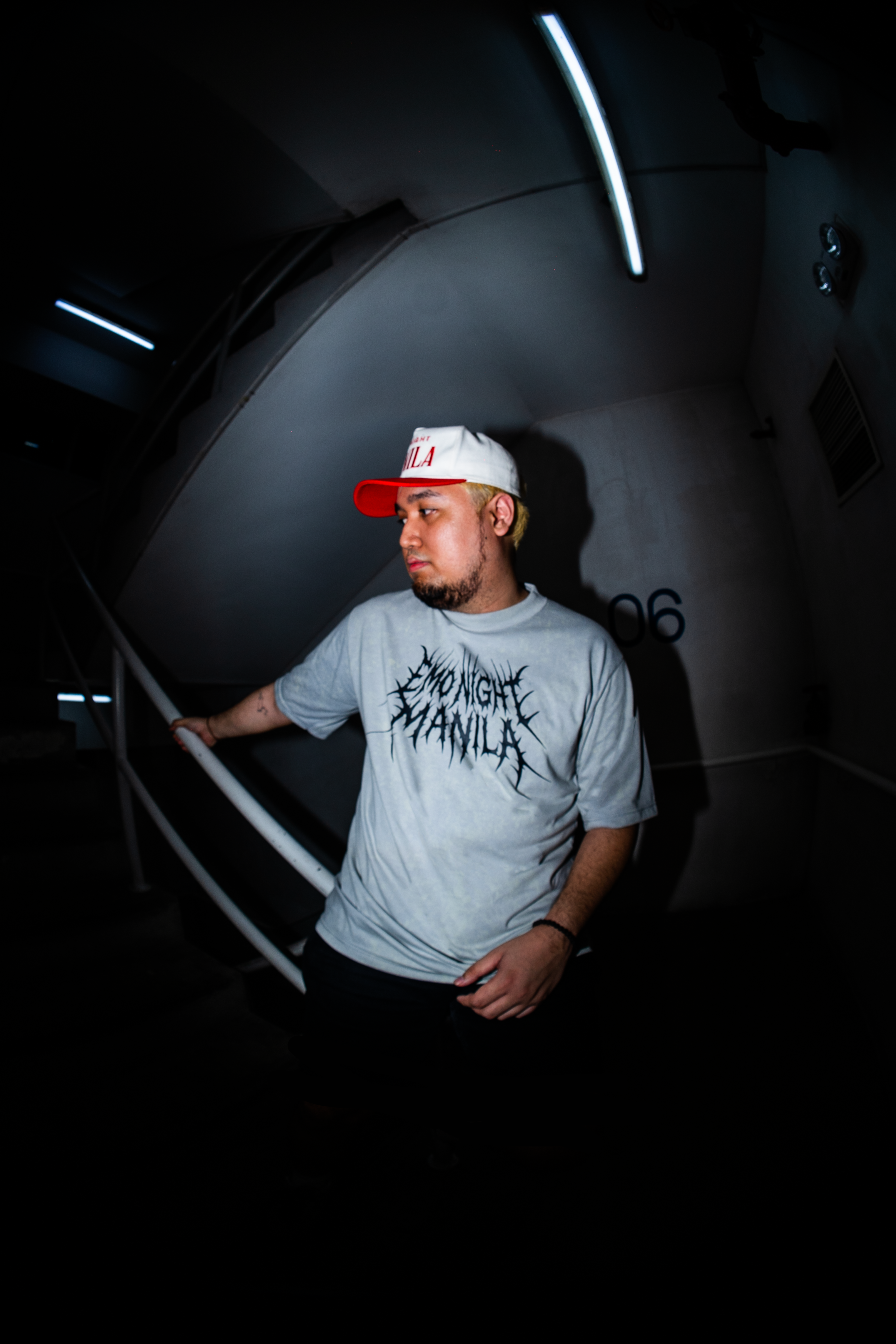 Person wearing a gray t-shirt with text and a cap in a dark room.